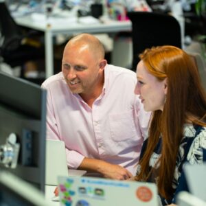 Two colleagues collaborating at a desk in a modern office environment, smiling and engaged.