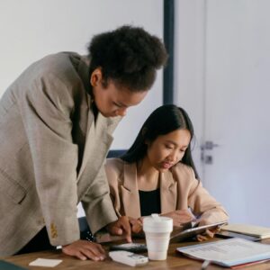 Two professional women working together in an office setting, focused on a project.