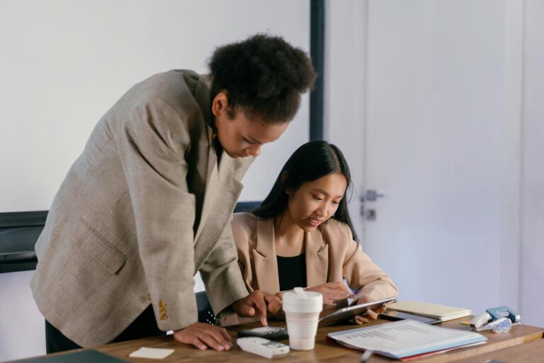 Two professional women working together in an office setting, focused on a project.